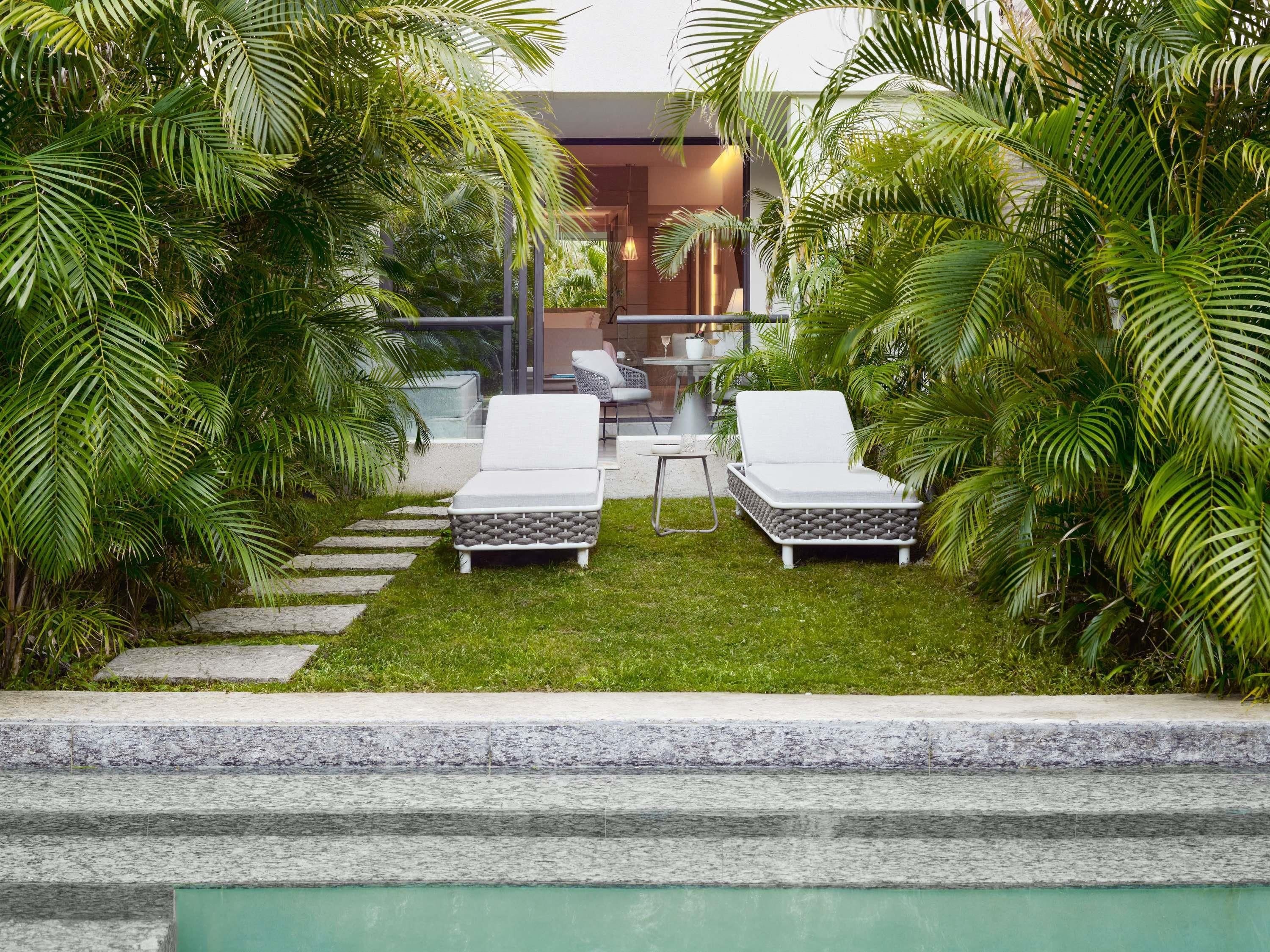 A modern outdoor lounge area with two white lounge chairs, a small table, and a glass balustrade.