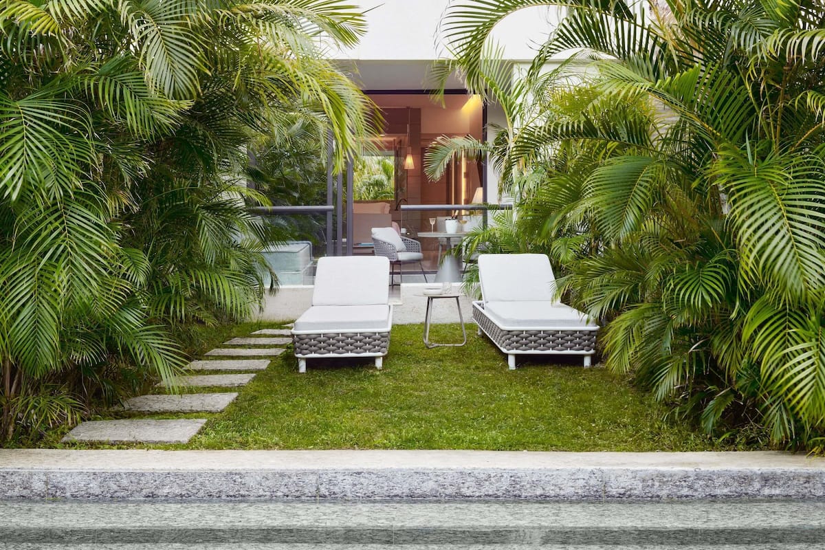 A modern outdoor lounge area with two white lounge chairs, a small table, and a glass balustrade.