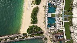 Vista aérea de un complejo turístico con piscina, playa y hotel contiguo.
