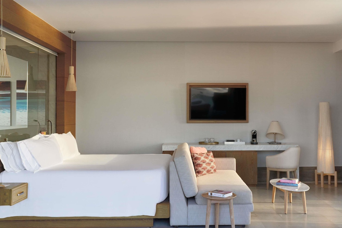 Una habitación de hotel moderna con una cama grande, un sofá, un escritorio y un televisor.