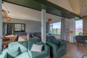 A spacious living area with a wooden dining table, green sofas, and a view of the outdoors.