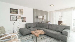 A modern living room with a grey sectional sofa, a wooden coffee table, and various framed artworks on the walls. - Strandleven 106 Apartment in Groote Keeten (Callantsoog)