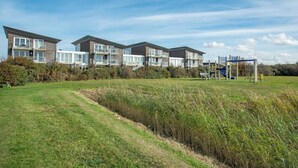 A row of modern multi-story buildings with large windows and balconies, surrounded by a grassy field and a playground. - Strandleven 106 Apartment in Groote Keeten (Callantsoog)