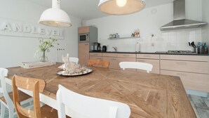 A modern kitchen with white cabinetry, a wooden dining table, and pendant lighting. - Strandleven 106 Apartment in Groote Keeten (Callantsoog)