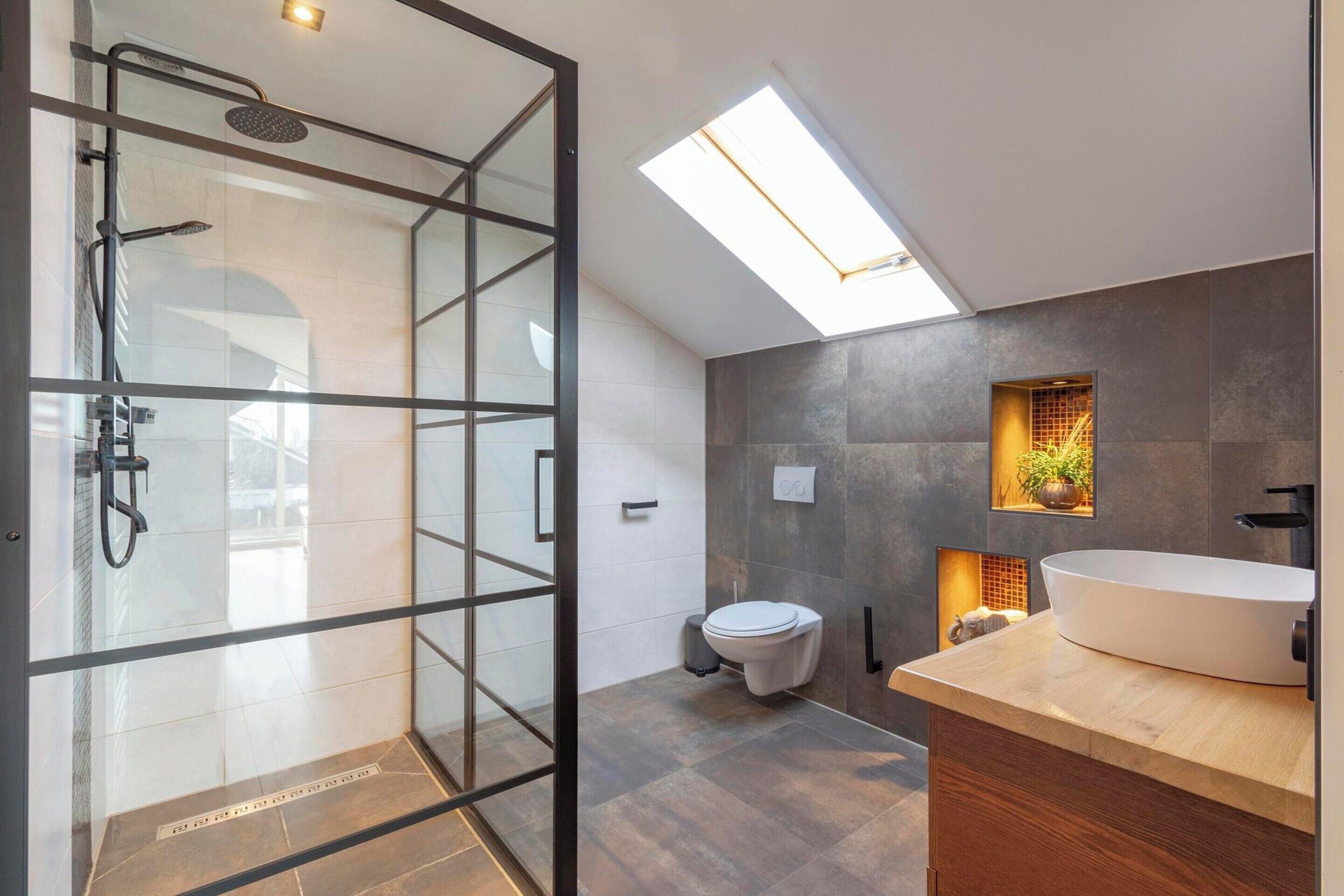 Un bagno moderno con finestra a lucernario, box doccia in vetro, un water e un lavandino grande.