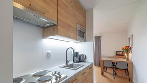 Une cuisine moderne équipée d’un four à micro-ondes encastré, d’un évier en acier inoxydable et d’une machine à café. Un coin repas avec une table et des chaises est également disponible.