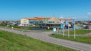 Un bâtiment moderne doté d’une structure centrale en verre, d’une entrée couverte et offrant une vue sur le front de mer.