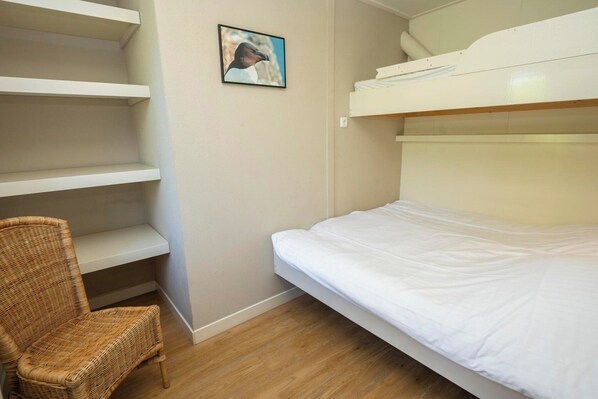 A bunk bed with white bedding, a wicker chair, and a shelf unit against a wall. - Apartment in De Koog Near Texel Beach (De Koog)