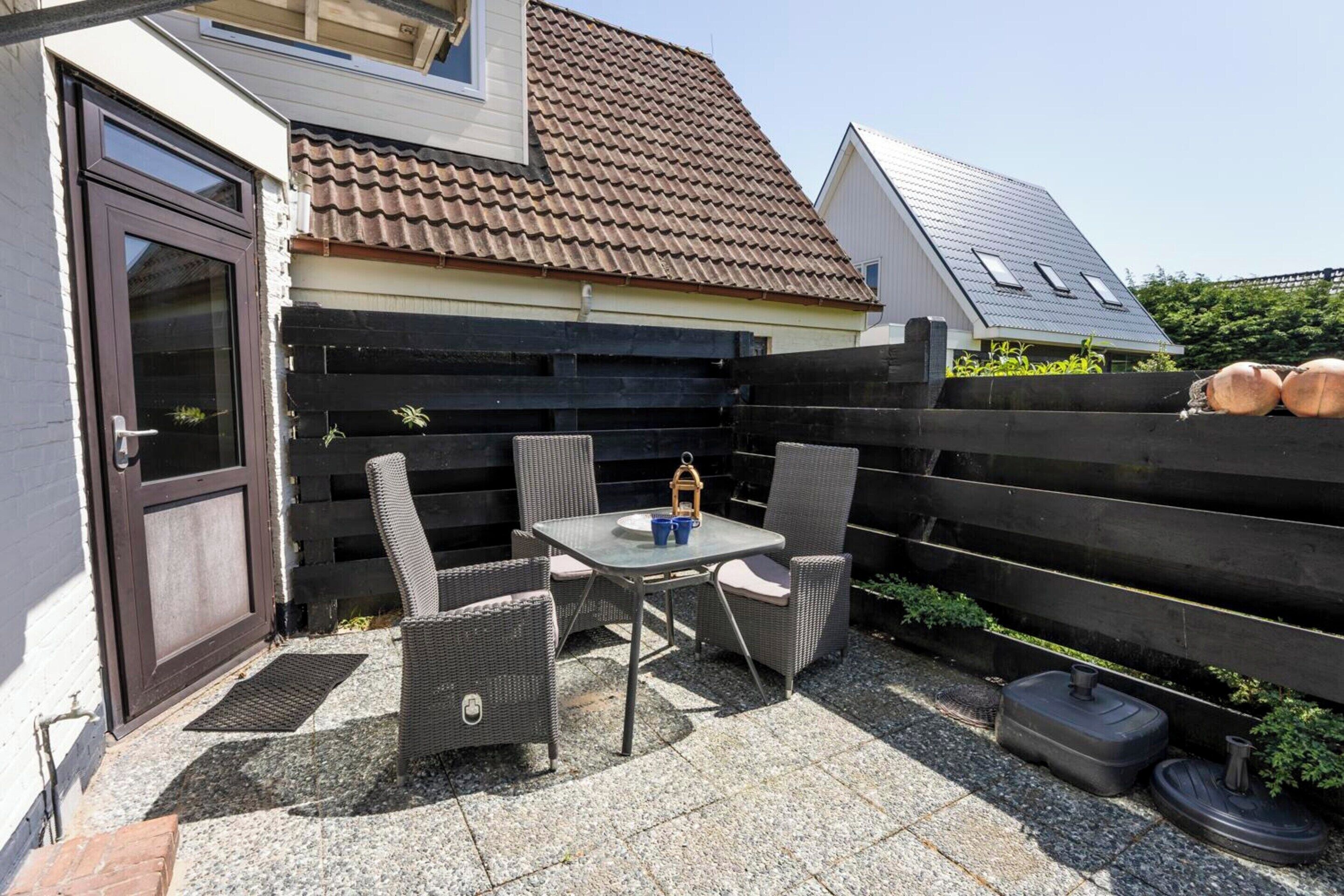 Eine Terrasse mit Tisch, Stühlen, einer Tür und einem Zaun.