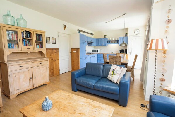 A cozy living room with a blue sofa, wooden cabinets, and a kitchen in the background. - Apartment in De Koog Near Texel Beach (De Koog)