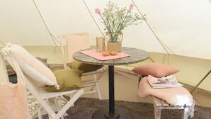 En mysig sittgrupp med ett runt bord, kuddar, en flätad korg och en vas med blommor.