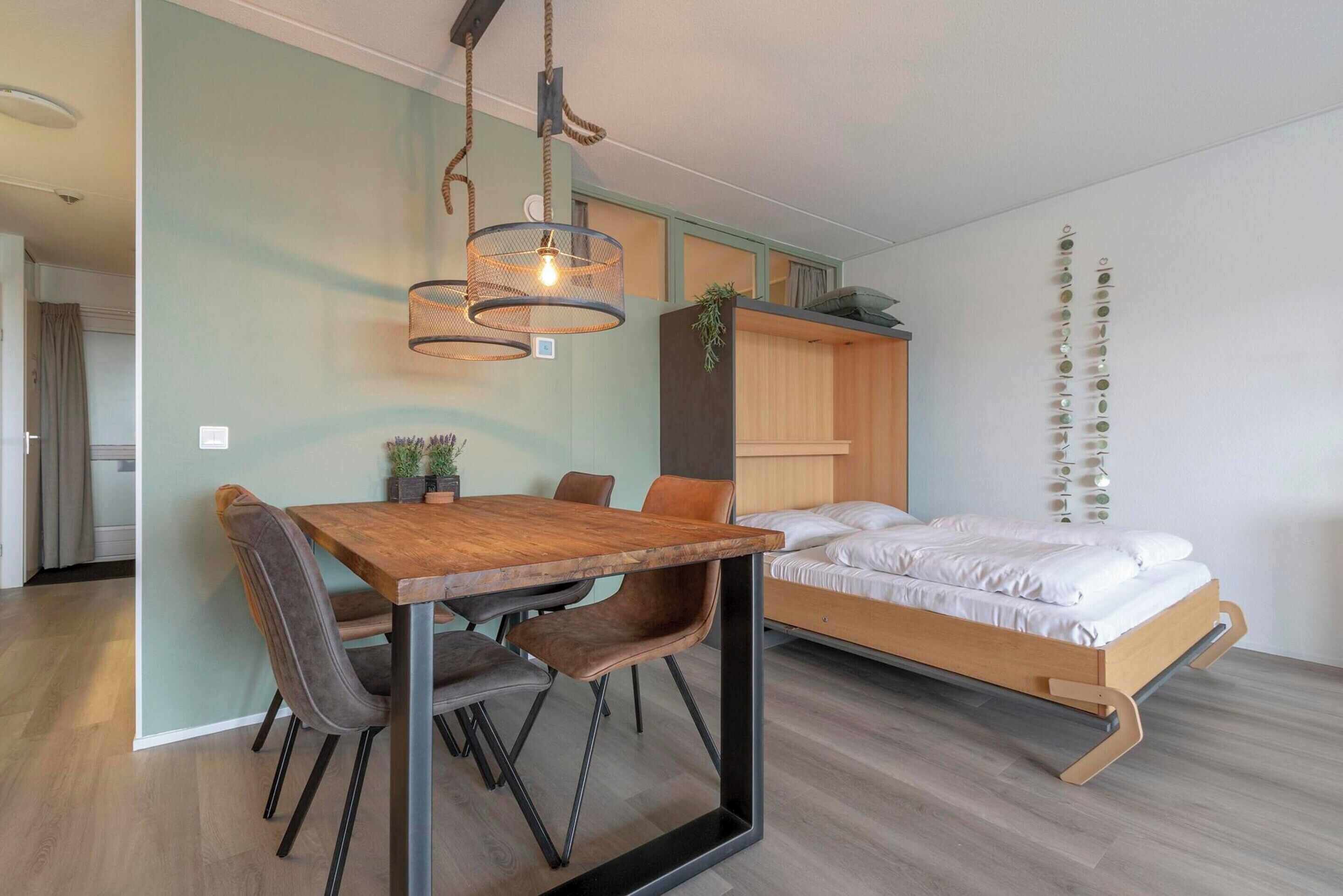 Une chambre à coucher moderne avec un lit en bois, une table à manger avec des chaises et un luminaire suspendu.