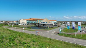 A modern building with a unique dome structure, a waterfront view, and multiple flags. - Strandslag 203 With Dunes View Balcony (Julianadorp)
