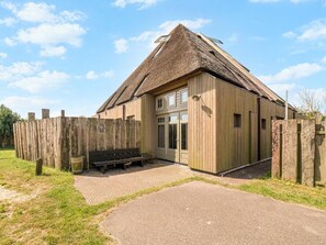A wooden building with a thatched roof, a bench, and a paved entrance. - Spacious Apartment With Garden (Callantsoog)