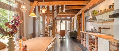 A spacious kitchen with a wooden ceiling, a dining area with a long table, and a view through the window.
