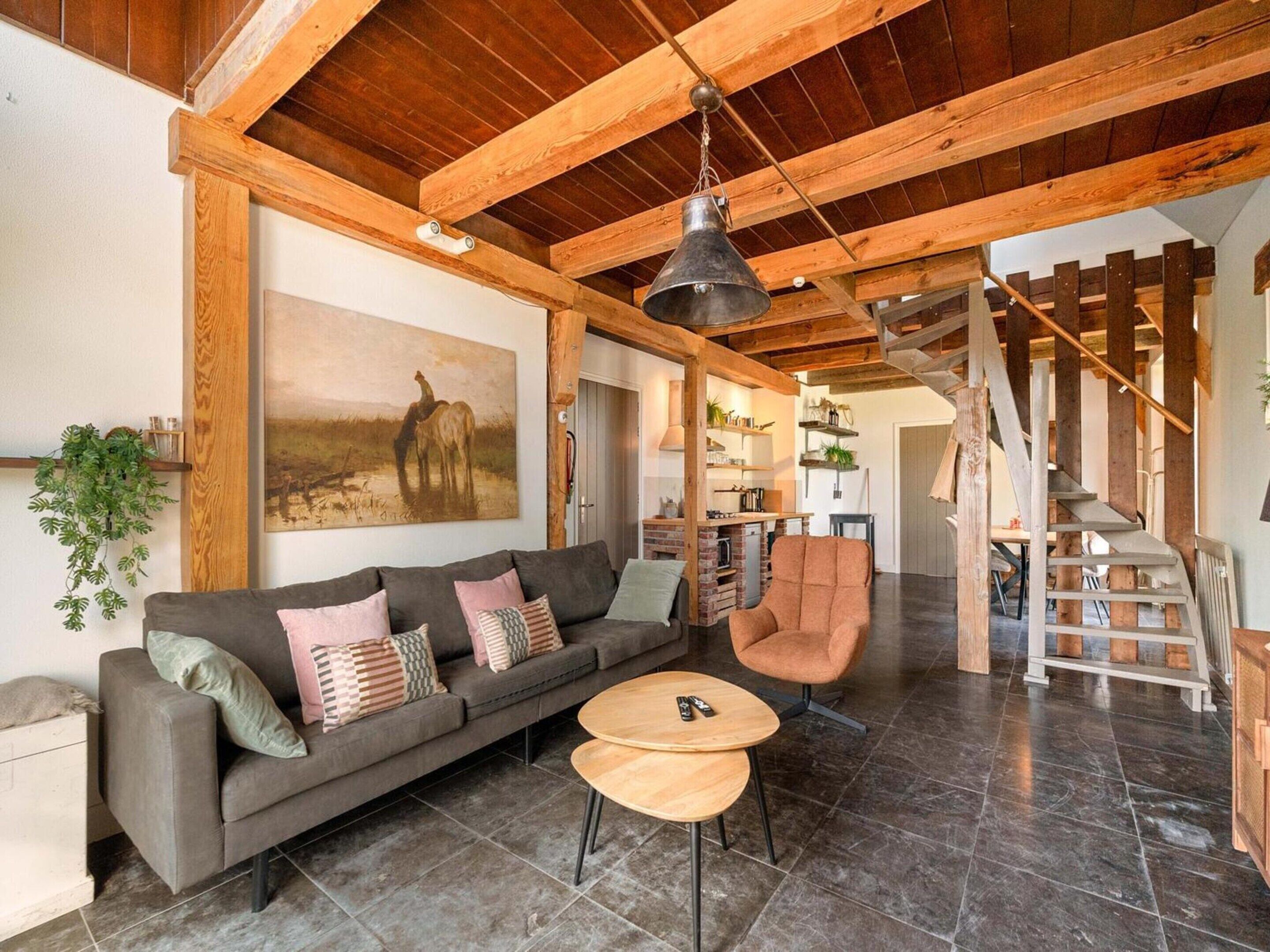 A spacious living area with a wooden ceiling, a sofa with cushions, a round wooden table, and a staircase with wooden railings.