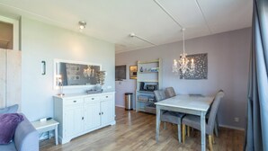 A modern living room with a dining area, white cabinetry, a chandelier, and a small trash can. - Strandslag 193 Charming Apartment for 4-person (Julianadorp)