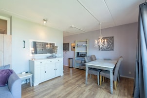 Una sala de estar moderna con comedor, muebles blancos, una lámpara de araña y un cubo de basura pequeño.