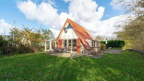 A modern house with a sloped roof, a patio with outdoor furniture, and a well-maintained lawn. - Sandepark 93 Home Near Groote Keeten Beach (Callantsoog)