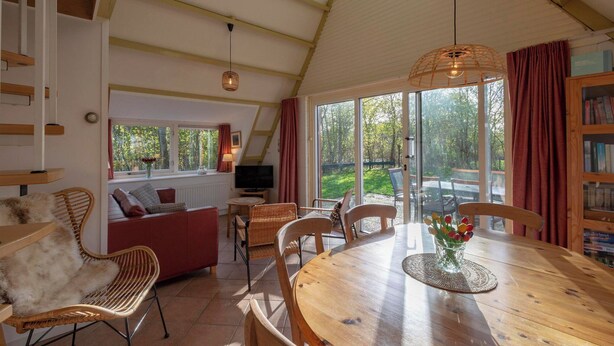 A cozy living room with a wooden dining table, wicker chairs, a sofa, and a TV. - Sandepark 93 Home Near Groote Keeten Beach (Callantsoog)