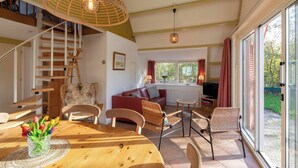 A spacious living area with a wooden staircase, a red sofa, wicker chairs, and a dining table with a vase of tulips. - Sandepark 93 Home Near Groote Keeten Beach (Callantsoog)