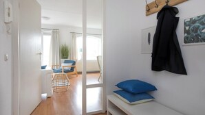A modern room with a wooden floor, a bench with blue cushions, a coat rack with a black coat, and a door leading to another room. - Residence Juliana 40 With Dune Views (Julianadorp)
