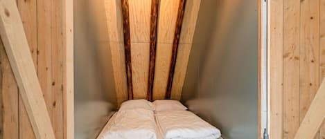 A wooden loft bedroom with a sloped ceiling, a single bed, and a wooden door.