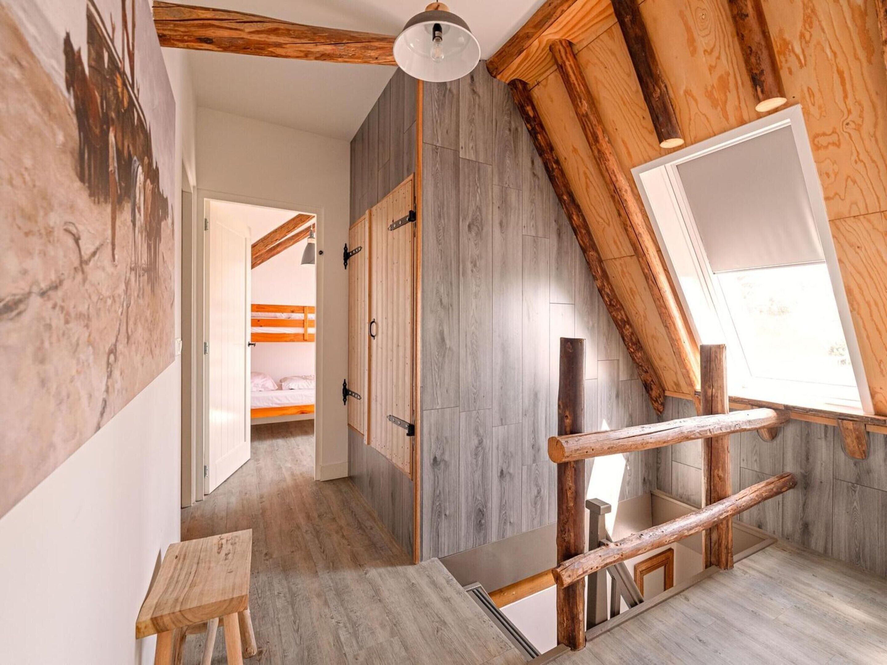 Una habitación con techo inclinado, vigas de madera, una cama litera, una mesita y un ventanal grande.
