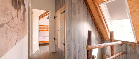 Een kamer met een schuine balkenplafond, een stapelbed, een klein tafeltje en een groot raam.