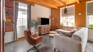 A cozy living room with a wooden ceiling, a television, a sofa, and a chair. - Apartment With Garden in Dutch Countryside (Callantsoog)