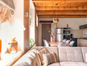 A modern kitchen with stainless steel appliances, a dining area with a wooden table and chairs, and a cozy living room with a sofa and cushions. - Apartment With Garden in Dutch Countryside (Callantsoog)