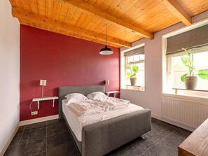 A bedroom with a bed, bedside lamps, a window with plants, and a wooden ceiling. - Apartment With Garden in Dutch Countryside (Callantsoog)
