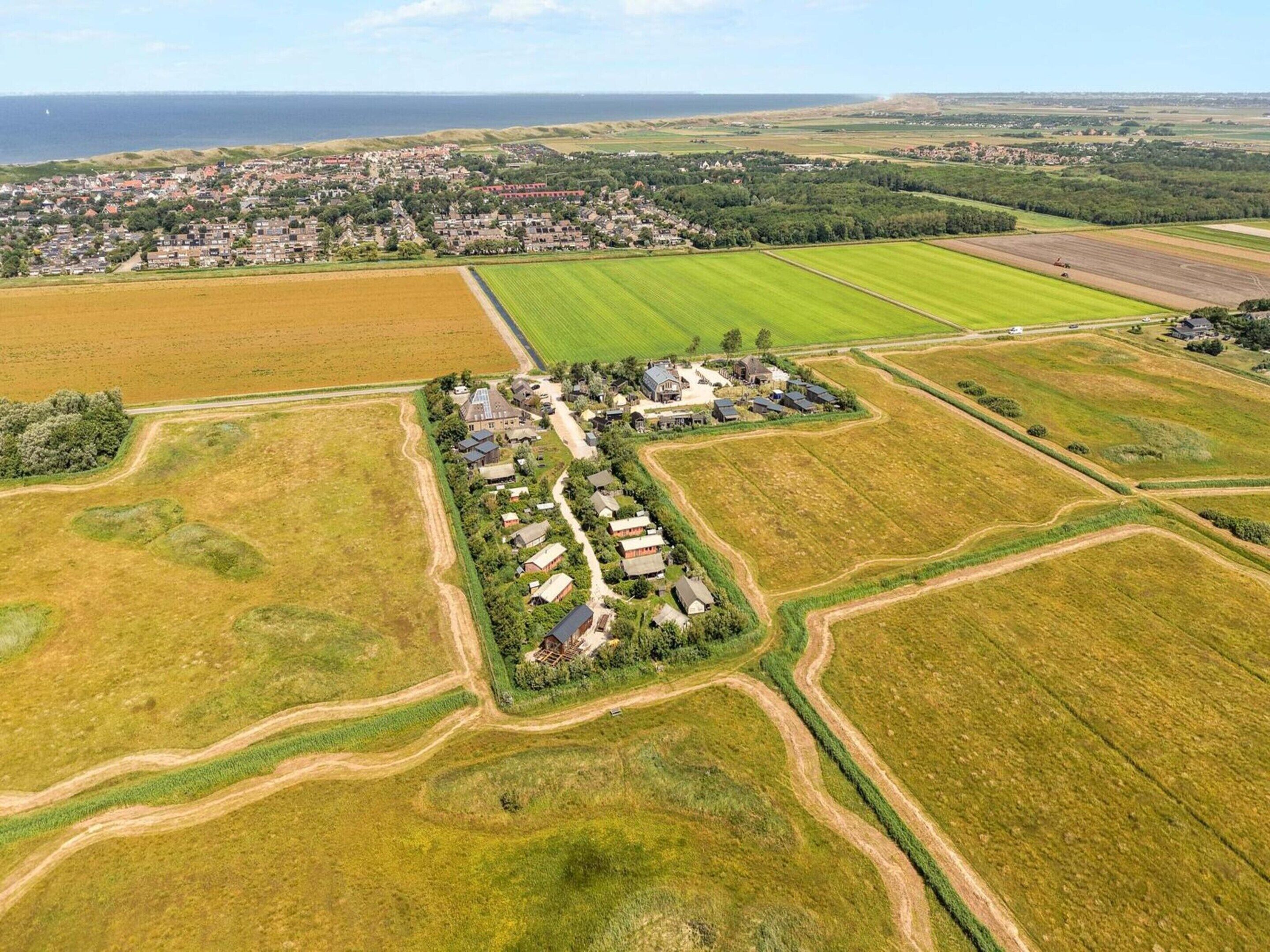 An aerial view of a rural area with fields, a small cluster of houses, and a distant town.