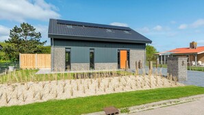 A modern two-story house with a sloped roof, solar panels, and a well-maintained garden with young trees and a gravel path. - Villa Near North Holland Beach With Jacuzzi (Julianadorp)