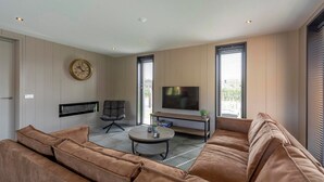 A modern living room with a sofa, a coffee table, a TV, and a clock on the wall. - Villa Near North Holland Beach With Jacuzzi (Julianadorp)