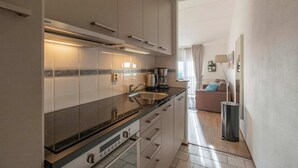 Una cocina moderna con estufa integrada, un fregadero y una cafetera. Hay un cubo de basura y una ventana con cortinas.