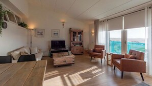 Amplia sala de estar con una mesa de centro de madera, un sofá y un televisor. Se observa un mueble de madera y un balcón con vistas.