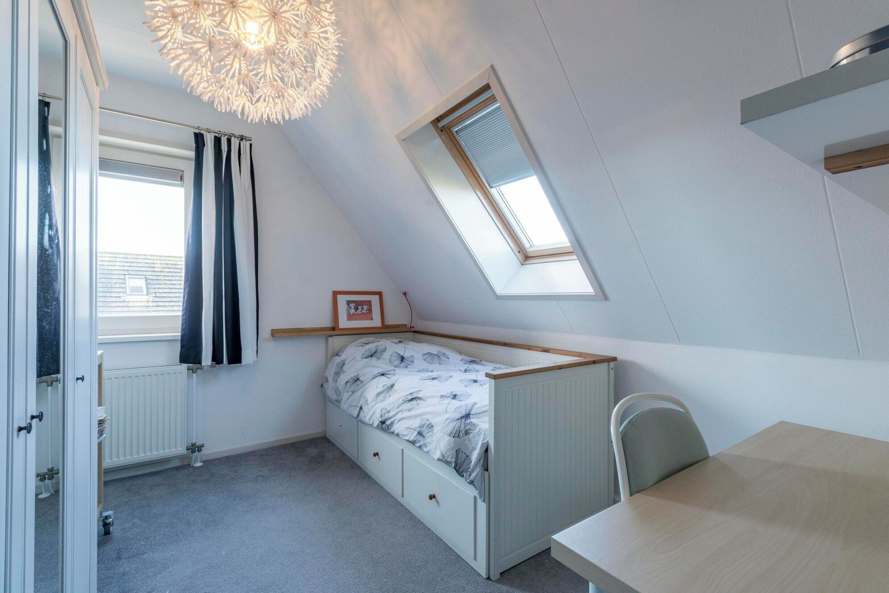 A bedroom with a sloped ceiling, a skylight, a bed with storage drawers, a radiator, and a table.