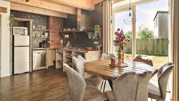 A modern kitchen with a dining area, wooden beams, and a view of the outdoors. - Vossehoeck 3 Apartment With Nature Reserve View (Callantsoog)