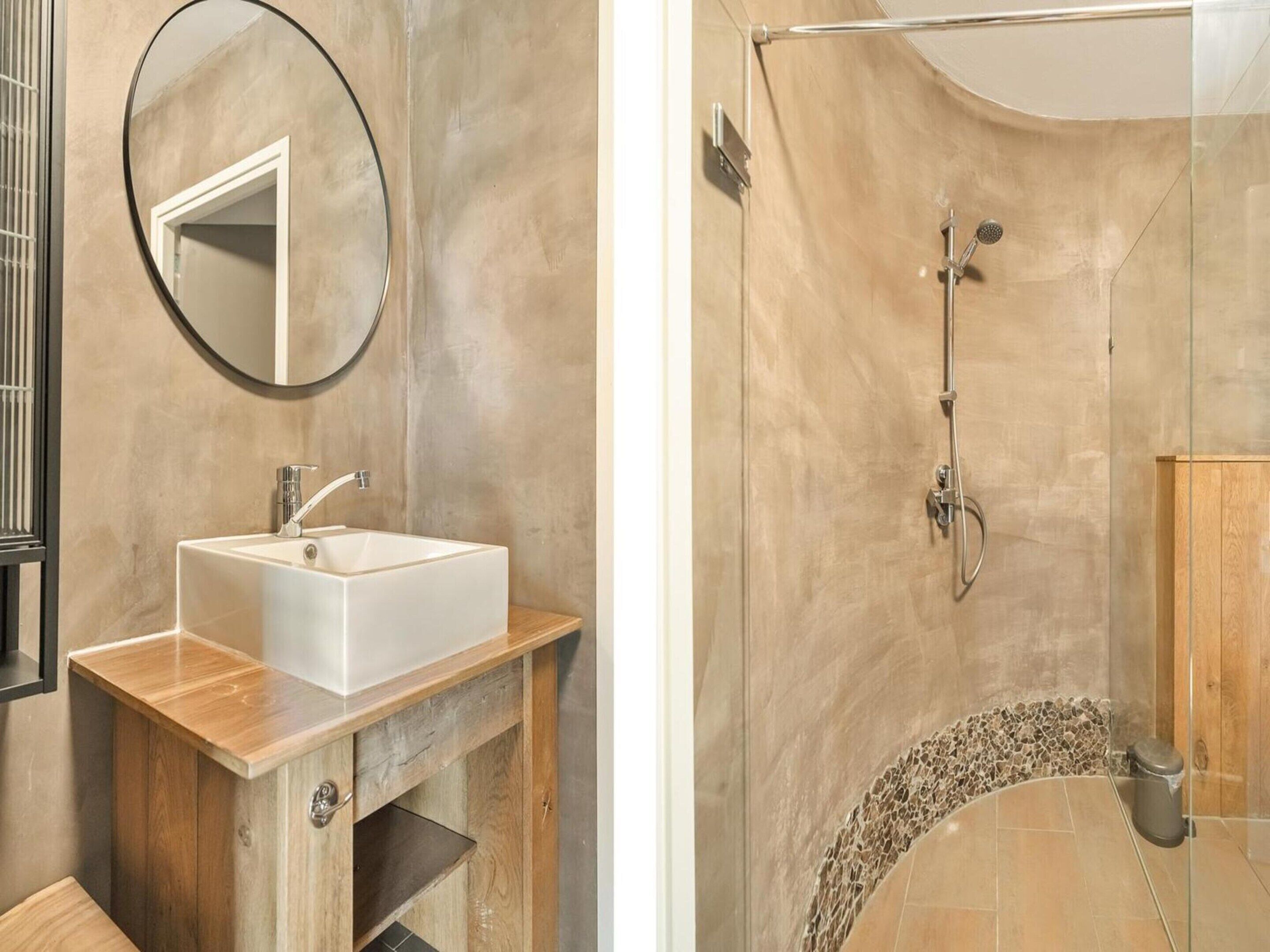 A bathroom with a white sink, a round mirror, and a shower with a glass door.