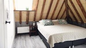 Een slaapkamer met een schuine kap, een bed met een gewatteerde spreideken, een nachtkastje met een lamp en een raam met uitzicht.