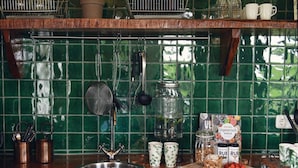A kitchen with a green tiled backsplash, hanging utensils, a stainless steel sink, and various kitchen items on the counter.