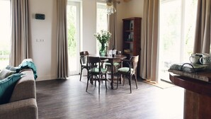 A dining area with a wooden table and chairs, a vase with flowers, and a bookshelf.