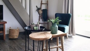 A room with a staircase, a blue armchair, a small round table, and potted plants. - Vossehoeck 4 Apartment in Callantsoog (Callantsoog)