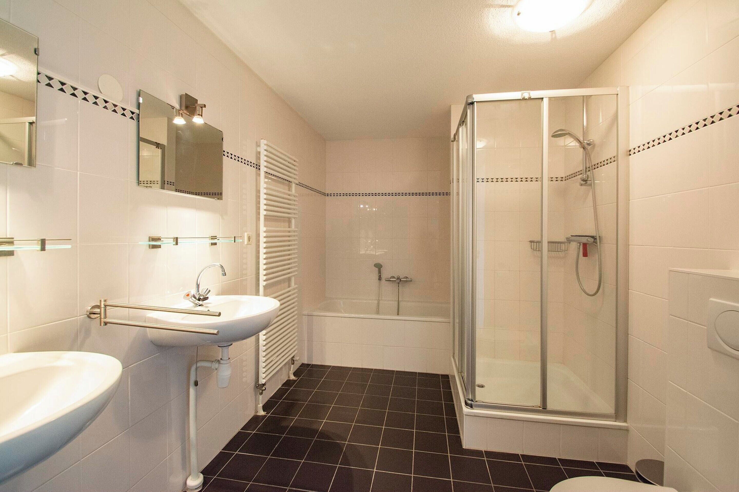 Een badkamer met een wastafel, spiegel en een douche met glazen wanden.