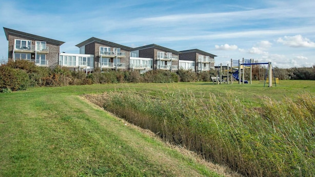 A row of modern multi-story buildings with large windows and balconies, surrounded by a grassy field and a playground. - Apartment in Groote Keeten Near Sandy Beach (Callantsoog)