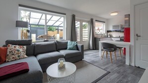 A modern living room with a grey sofa, a round coffee table, and a dining area with a white table and chairs. - Stuijvezandeweg 7Z for 2 Guests Near Centre (Callantsoog)