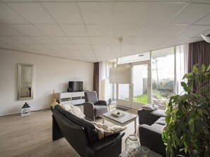 A modern living room with a sofa, armchairs, a coffee table, and a TV on a cabinet. - Strandslag 107 Apartment by the Beach (Julianadorp)