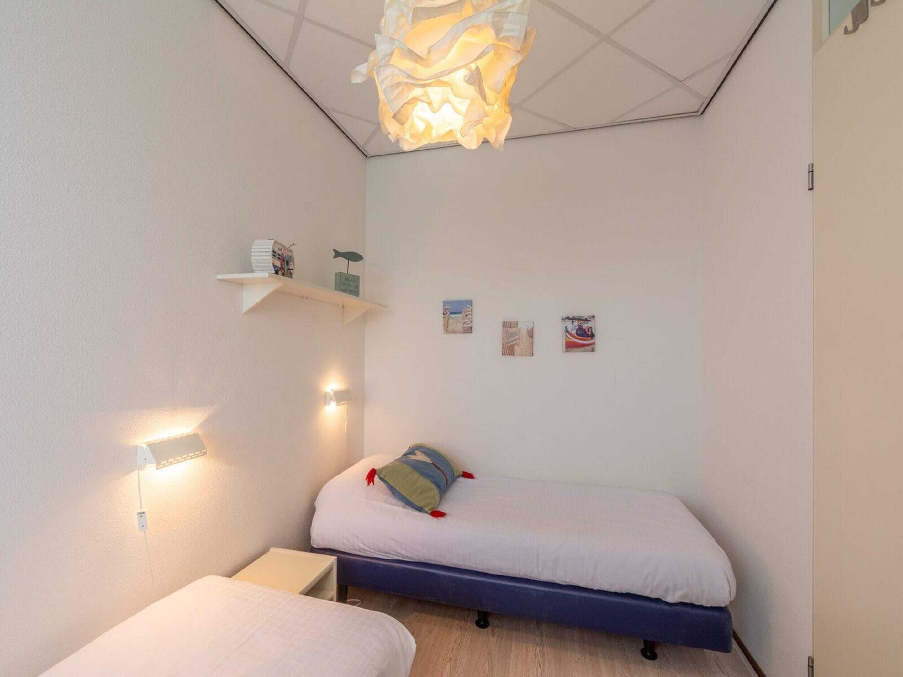A small, well-lit bedroom with a single bed, bedside tables, and wall-mounted shelves.