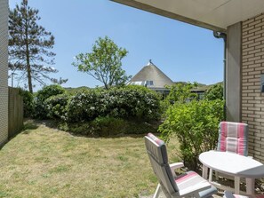 Eine Terrasse mit Stuhl und Tisch, eine Backsteinmauer und Blick auf ein Haus mit einem Kegeldach.